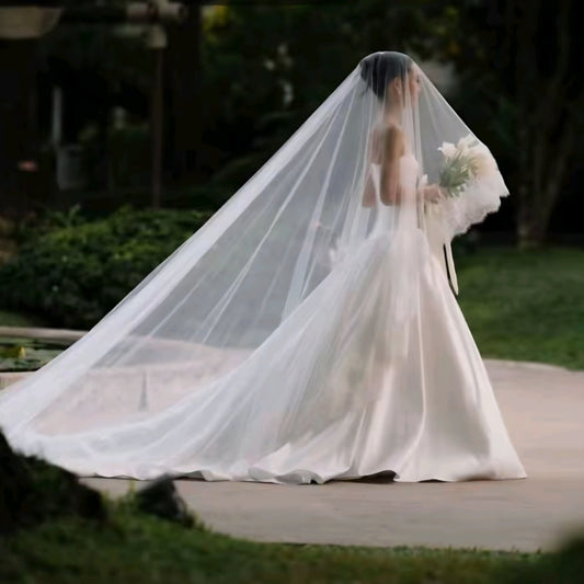 Bride in a white wedding dress with a long veil and bouquet, standing outdoors.